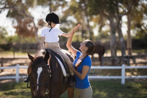 Seitenansicht einer Frau, die einem auf dem Pferd sitzenden Mädchen ein High Five gibt.